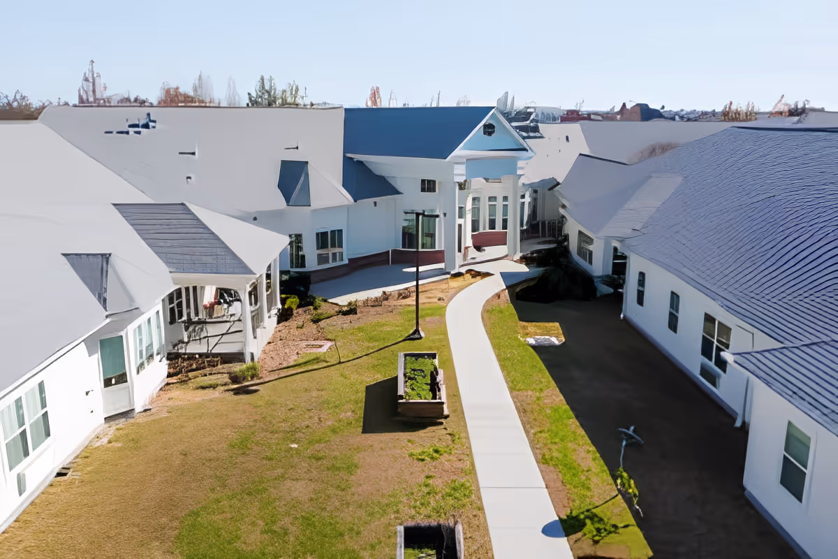 Aerial view of white senior living buildings surrounding a central courtyard with a curved sidewalk leading to a columned main entrance.