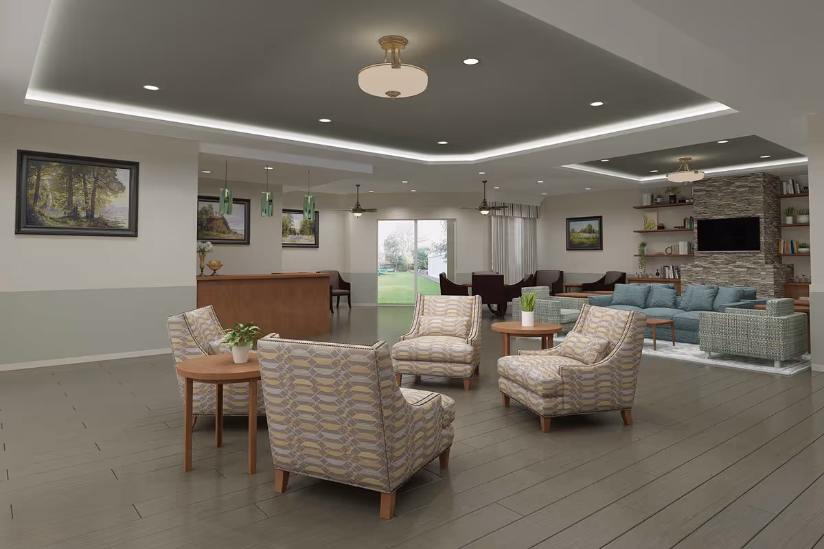 A spacious and modern living room area in a senior living facility with patterned armchairs arranged around small wooden tables, a teal sofa set near a stone fireplace with a mounted TV, built-in shelves with books and plants, ceiling fans, recessed lighting, and large windows showing a green outdoor space.