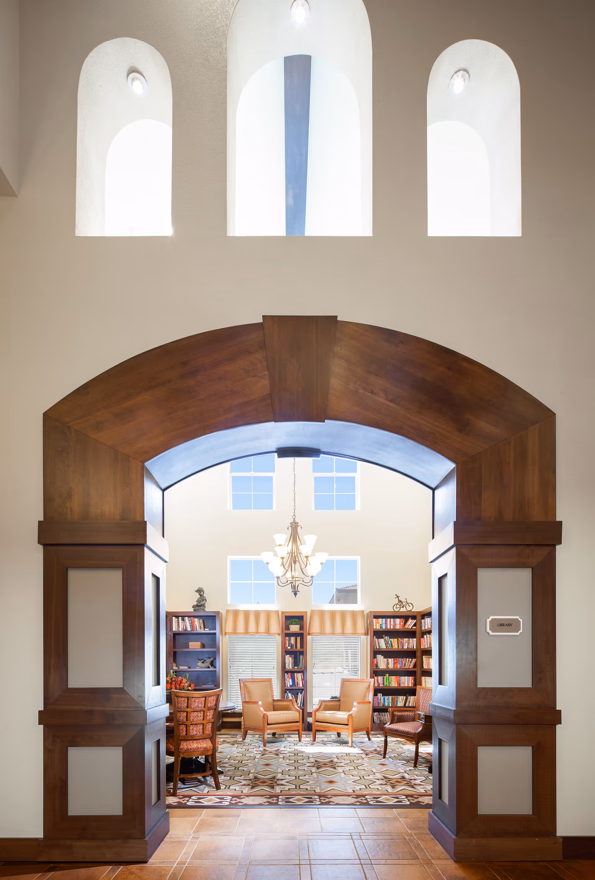 Wood-framed arched entryway opening into a bright library/lounge with bookshelves, chairs, and a chandelier.