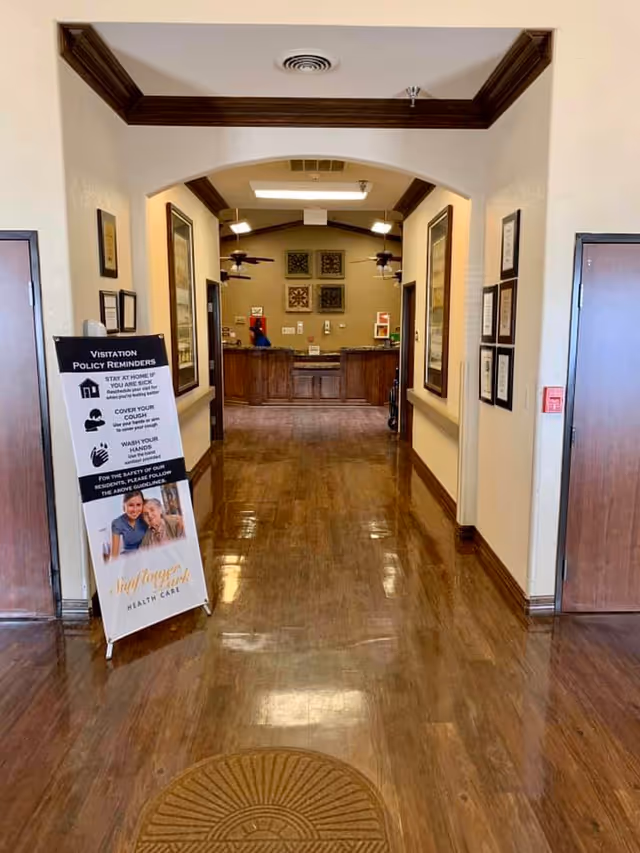 A polished wood-floored hallway leads to a reception desk with a freestanding visitation policy sign in the foreground.
