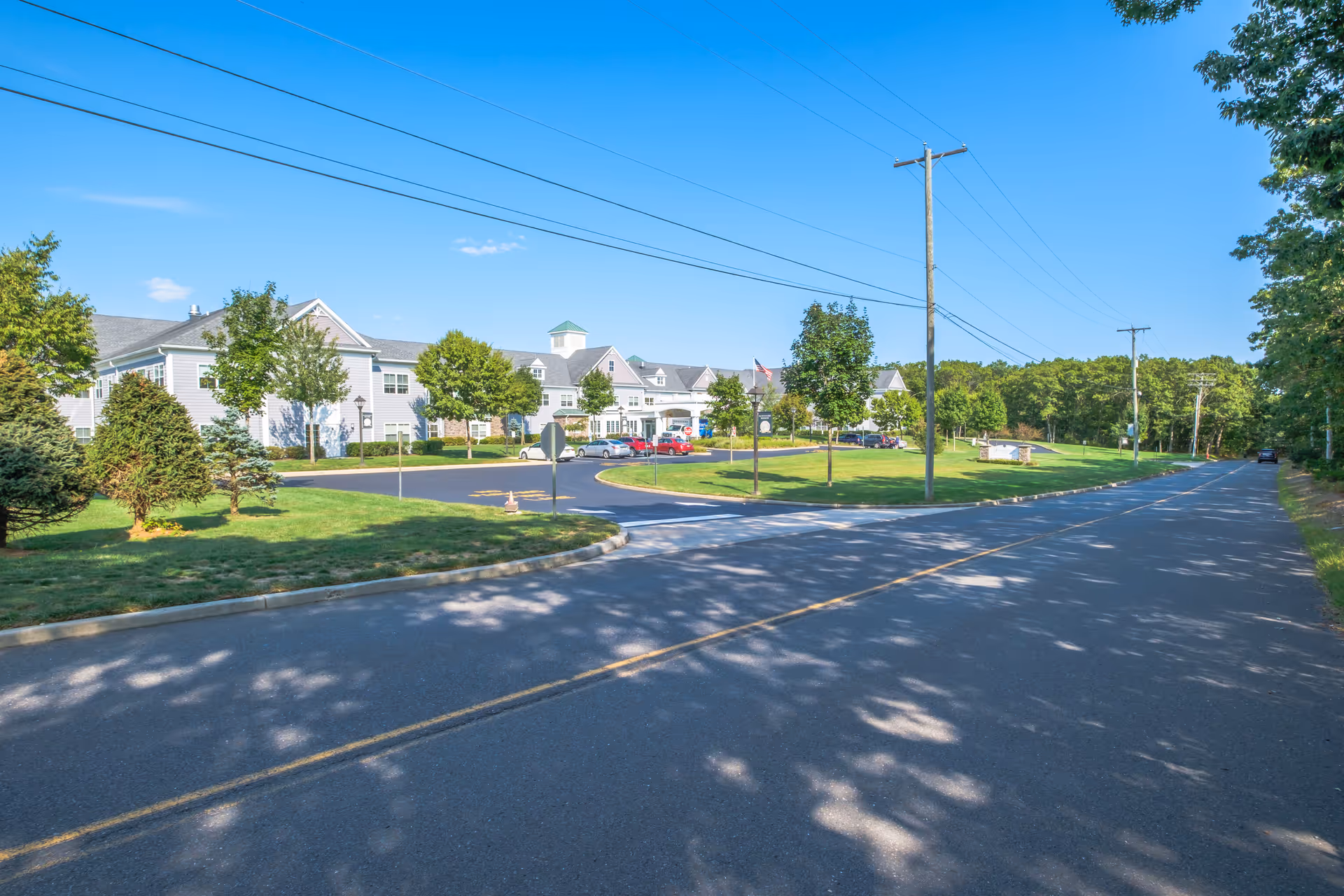 Wide exterior view of Sunnyside Manor's two-story white building with landscaped lawn and a road in front under a blue sky.