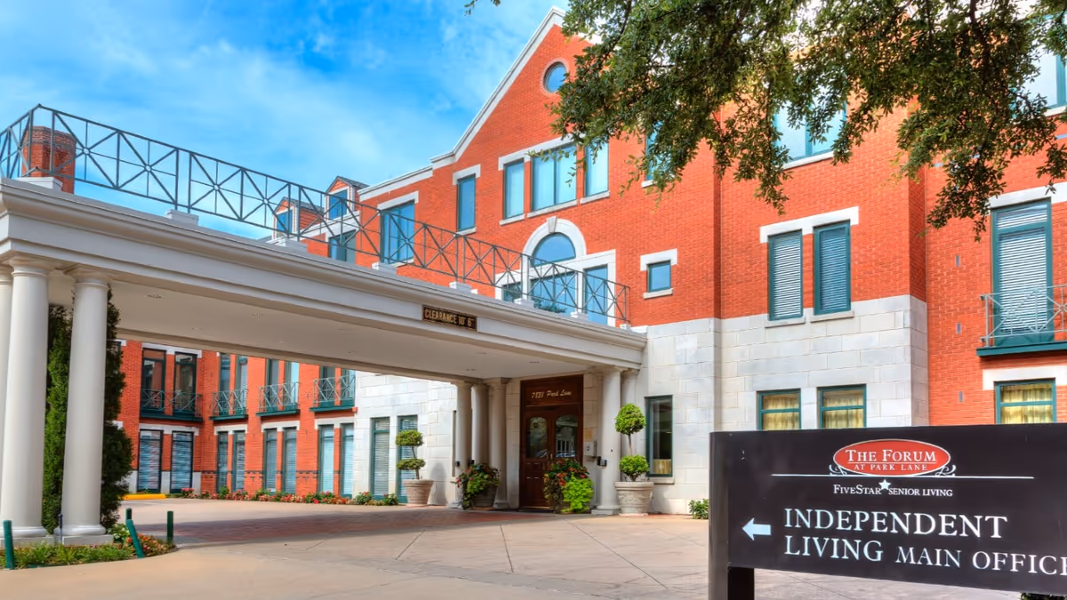 Front entrance and covered drive of a red-brick senior living building with landscaping and a sign for The Forum at Park Lane indicating the Independent Living main office.