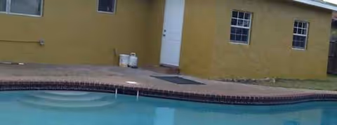 Exterior view of a yellow senior living facility with a pool in the foreground.