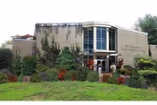 Exterior view of St Michael's Home, a two-story building with large windows and surrounded by well-maintained greenery and shrubs.