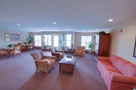 Spacious communal living room with sofas, armchairs, coffee tables and a dining area by large windows.