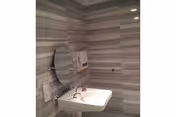 A small bathroom with gray and white striped tile walls, a white wall-mounted sink with a faucet, a round mirror above the sink, a soap dispenser mounted on the wall, and a hand dryer or paper towel dispenser next to the mirror.
