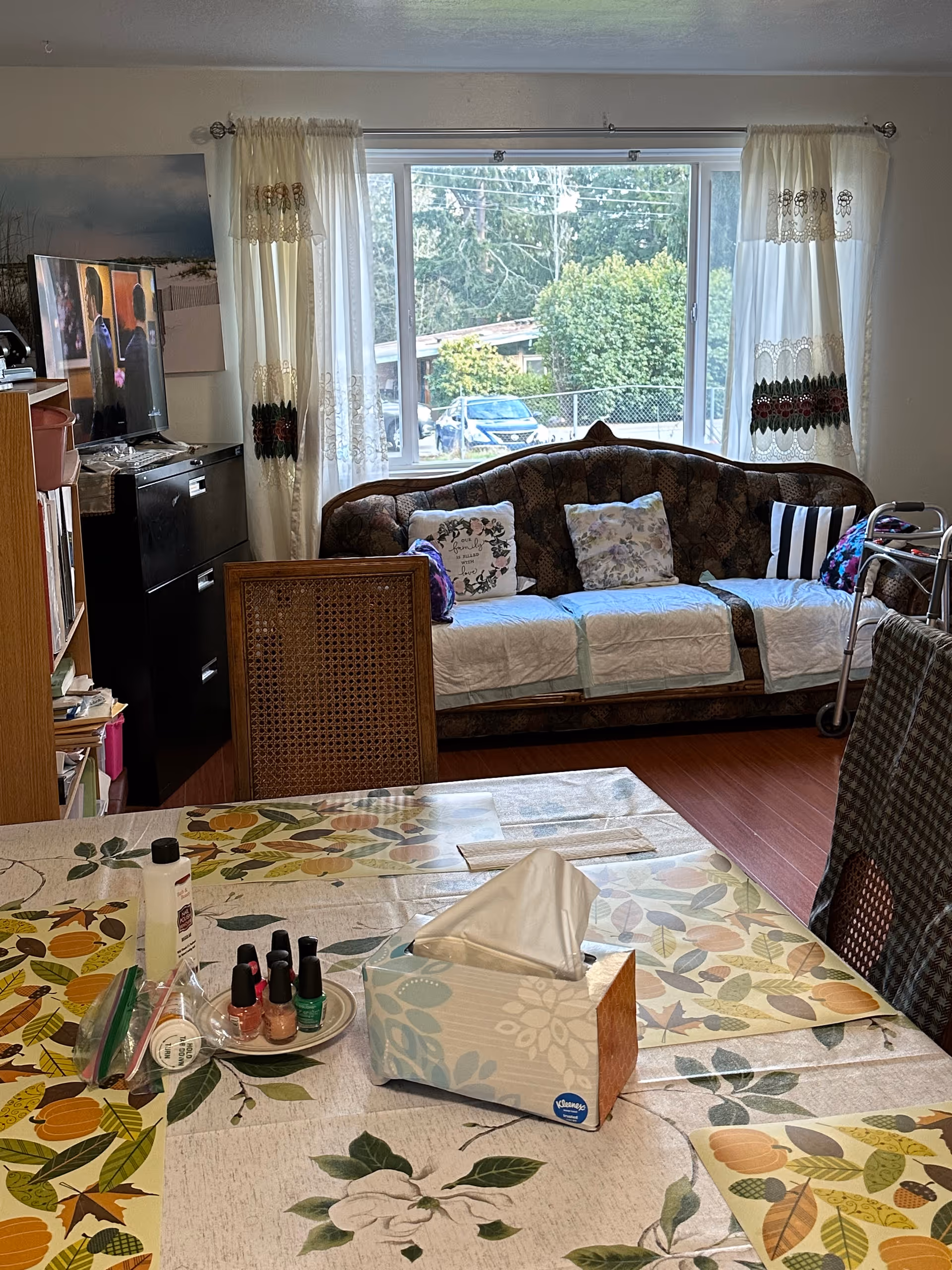 Indoor living area with a tissue-covered dining table in the foreground and a sofa with pillows by a large window in the background.