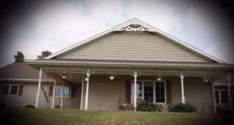 Front exterior of a single-story senior living facility with a covered porch and chairs.