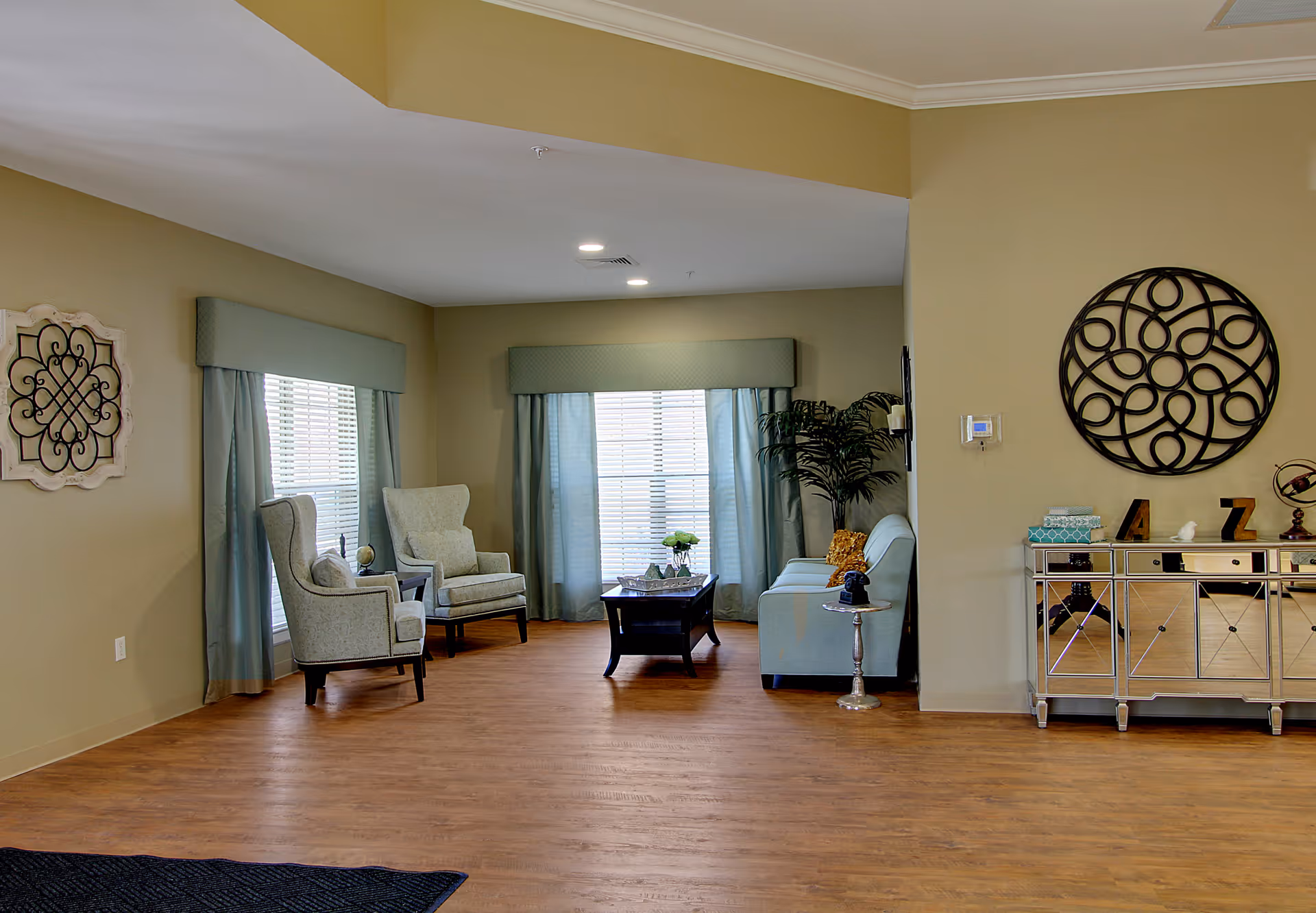 A spacious, well-lit living room with two upholstered armchairs, a sofa, a coffee table, decorative wall art, and a mirrored console.