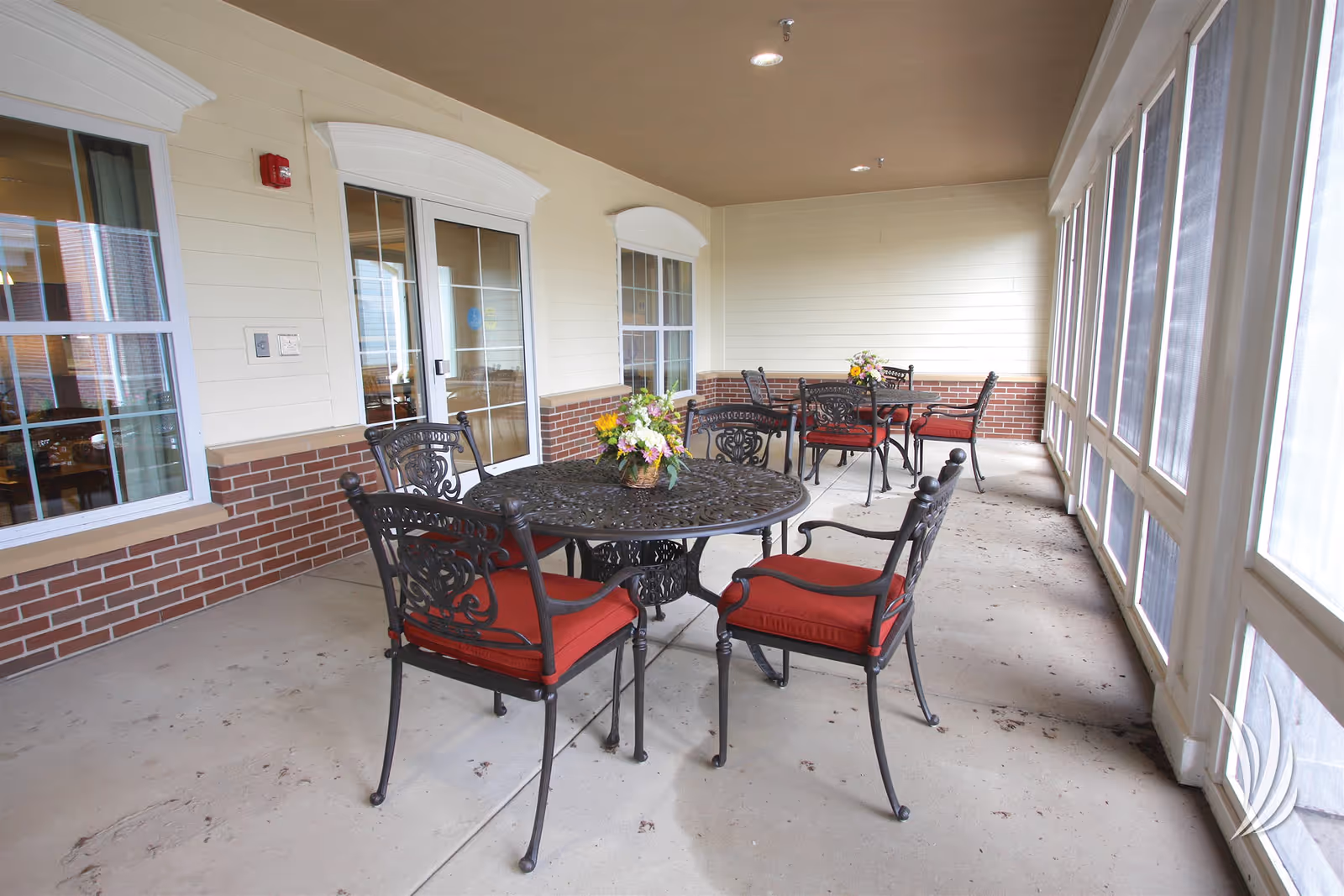 Screened outdoor patio with wrought-iron tables and red-cushioned chairs and floral centerpieces.