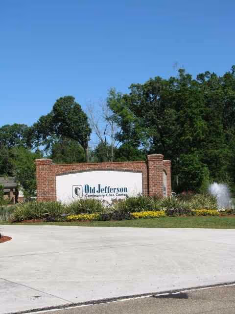 Brick sign for Old Jefferson Community Care Center with landscaped entrance and blue sky.