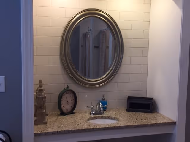 Bathroom vanity with an oval mirror, granite countertop, sink, faucet and decorative items.