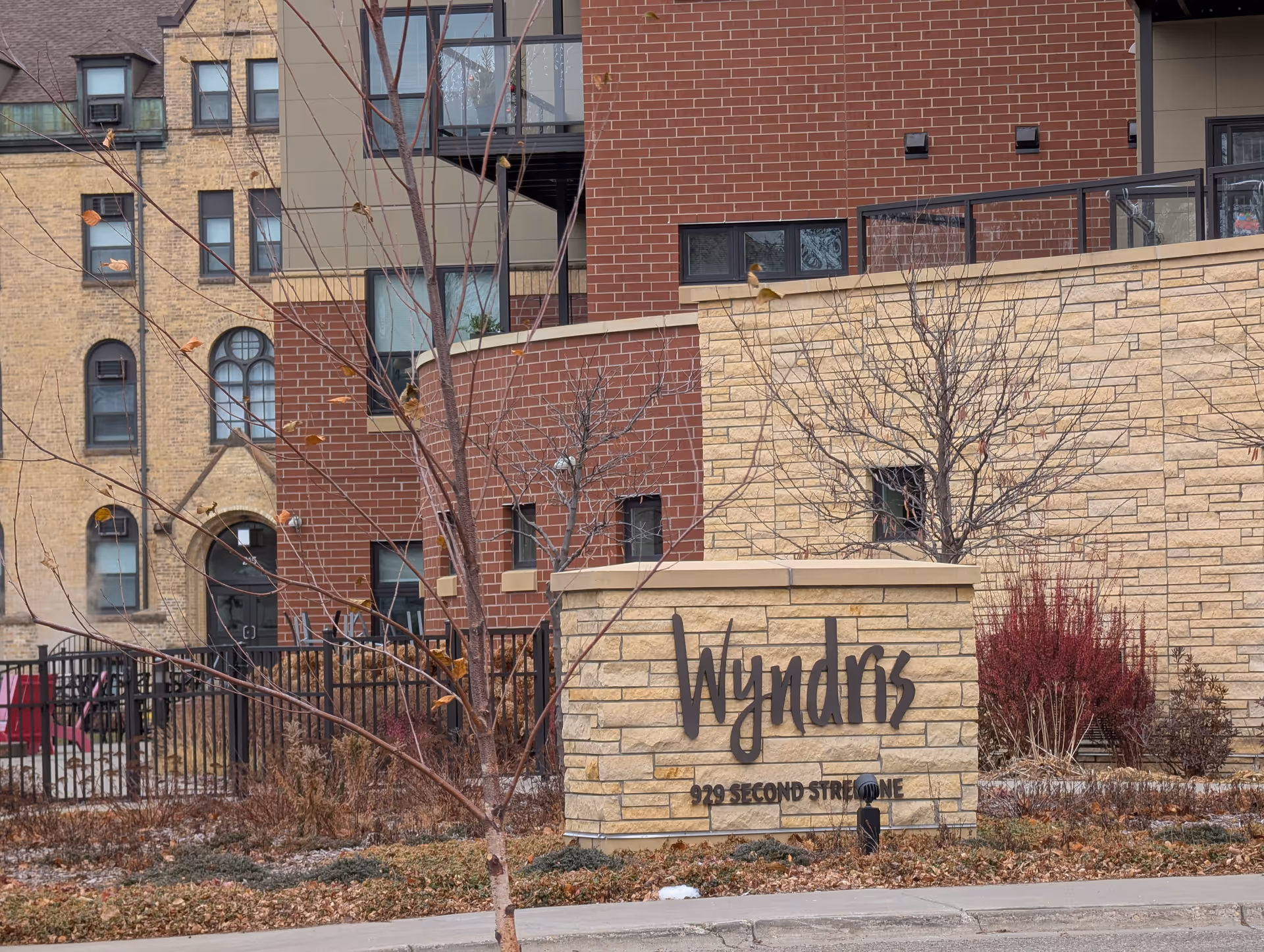 Exterior view of Wyndris, a Catholic Eldercare Community, showing a stone sign with the name and address 929 Second Street NE in front of a brick and stone building with leafless trees and landscaping.