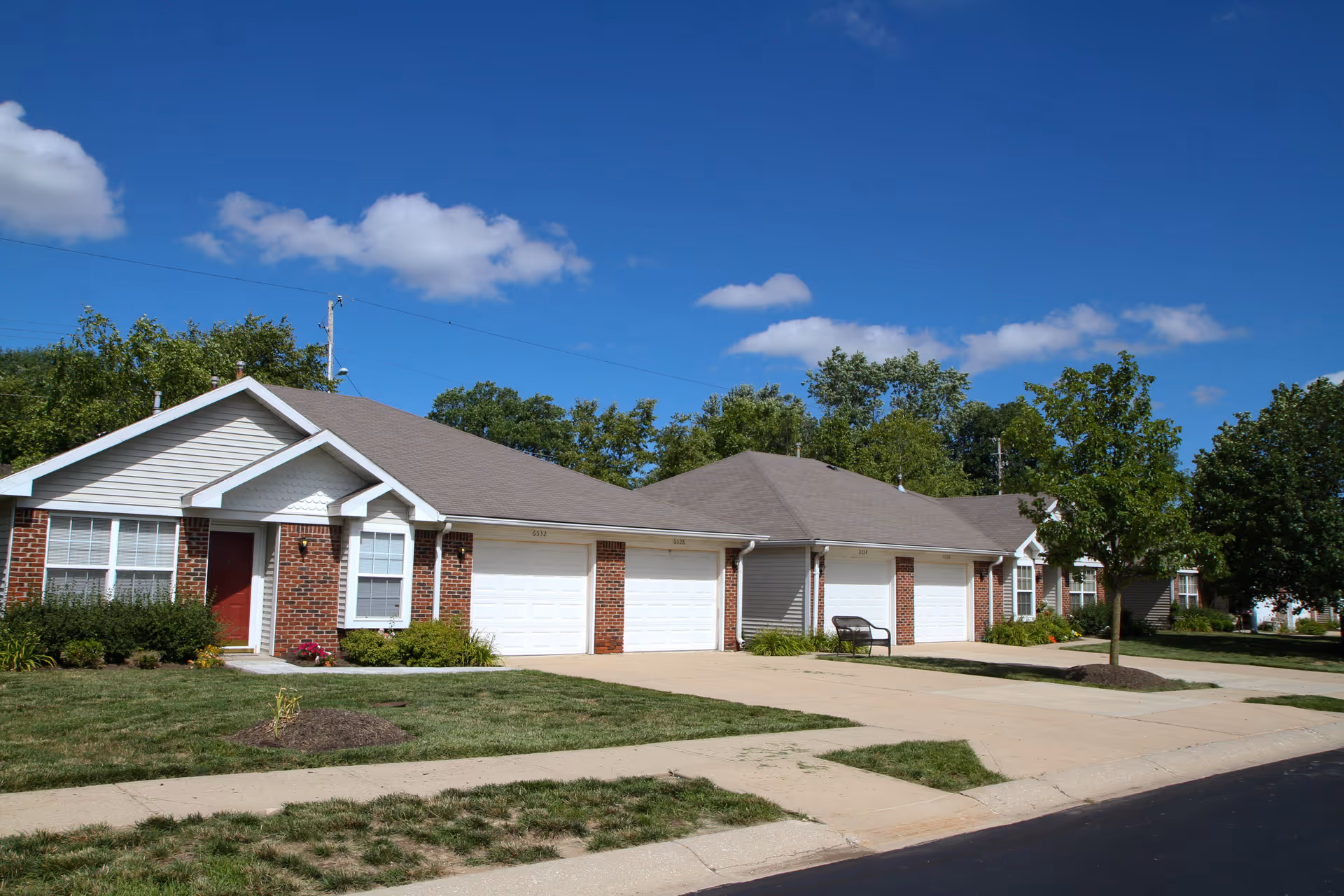 Single-story brick and siding residences with attached garages and driveways under a blue sky.