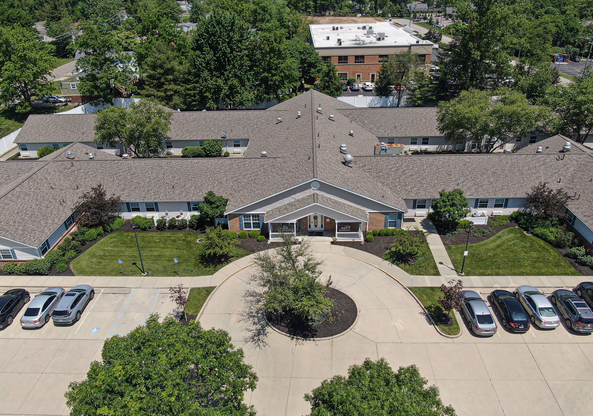 Aerial view of a single-story memory care facility with a circular driveway, parked cars, and landscaped lawns.