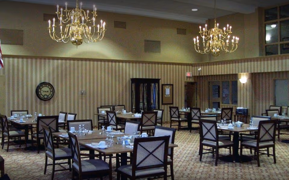 Spacious dining room with multiple tables and chairs set with dishes and chandeliers overhead.