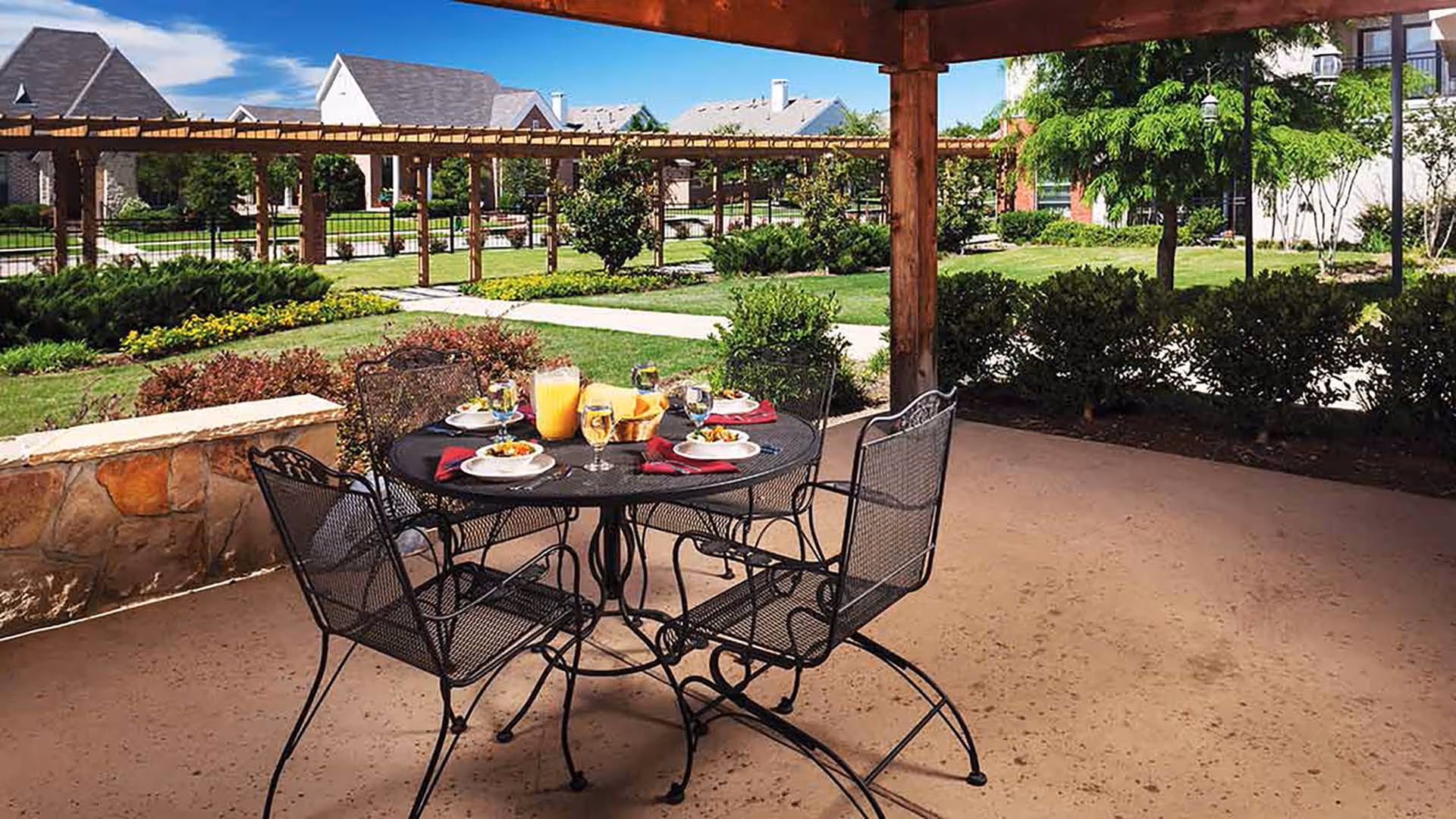 Outdoor covered patio with a metal dining table set for a meal overlooking a landscaped courtyard and pergola.