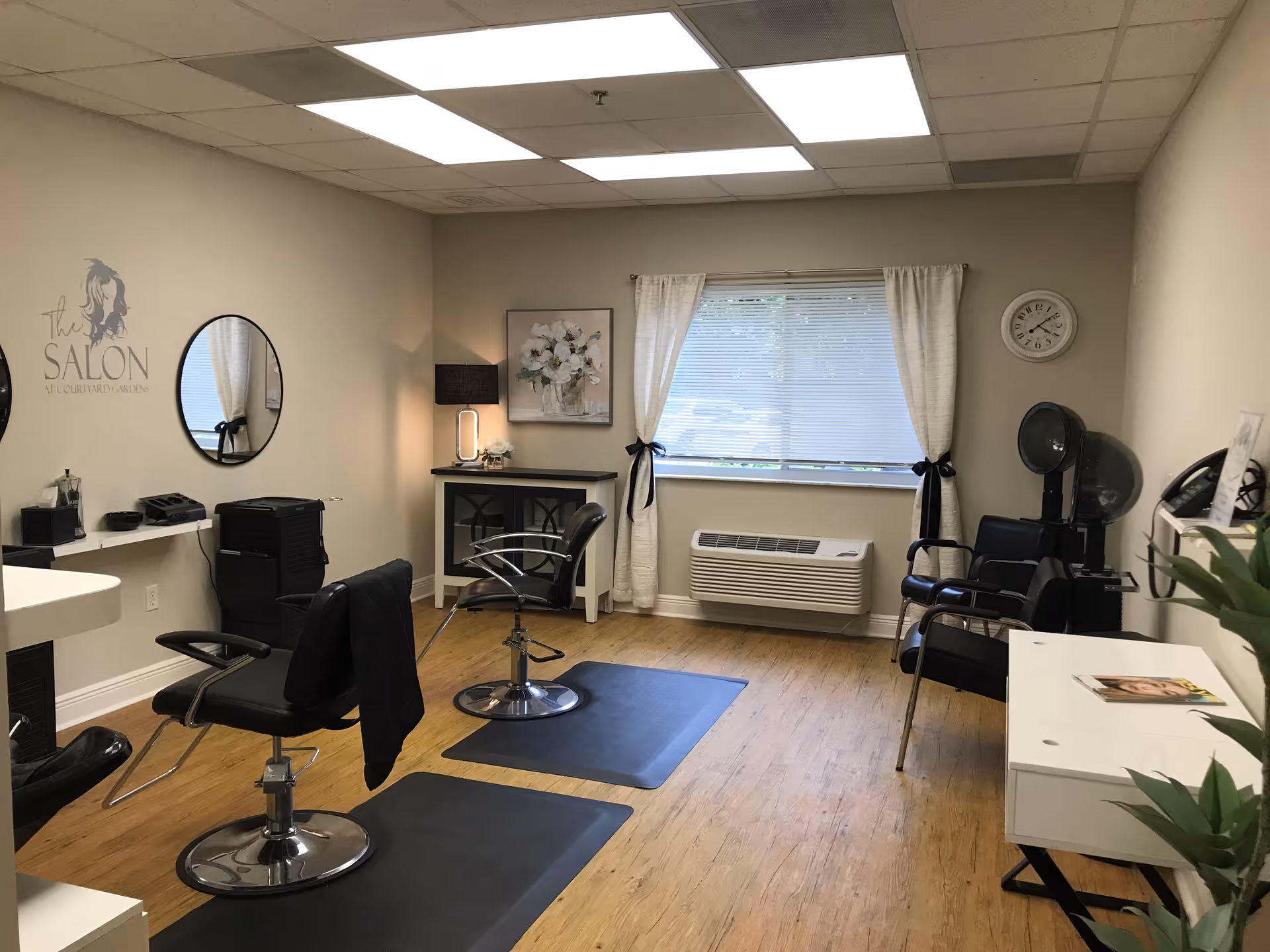 A small salon interior with styling chairs, mirrors, a window, and hair-drying stations.