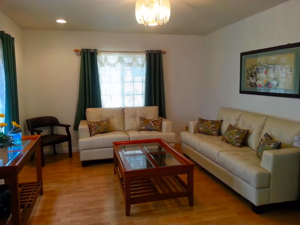 Well-lit living room with two cream sofas, a wooden coffee table, green curtains and framed wall art.