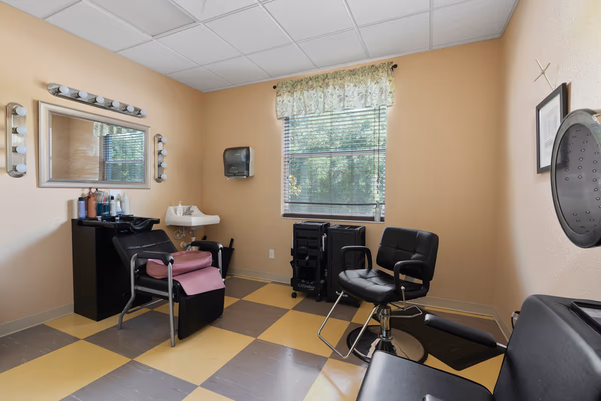 Small salon-style room with styling chairs, a shampoo sink, a lighted mirror, and a window.