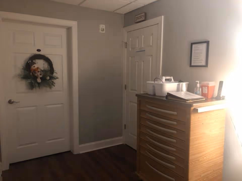 Small interior hallway with two closed white doors, one decorated with a wreath, and a wooden drawer cabinet topped with medical supplies and paperwork.