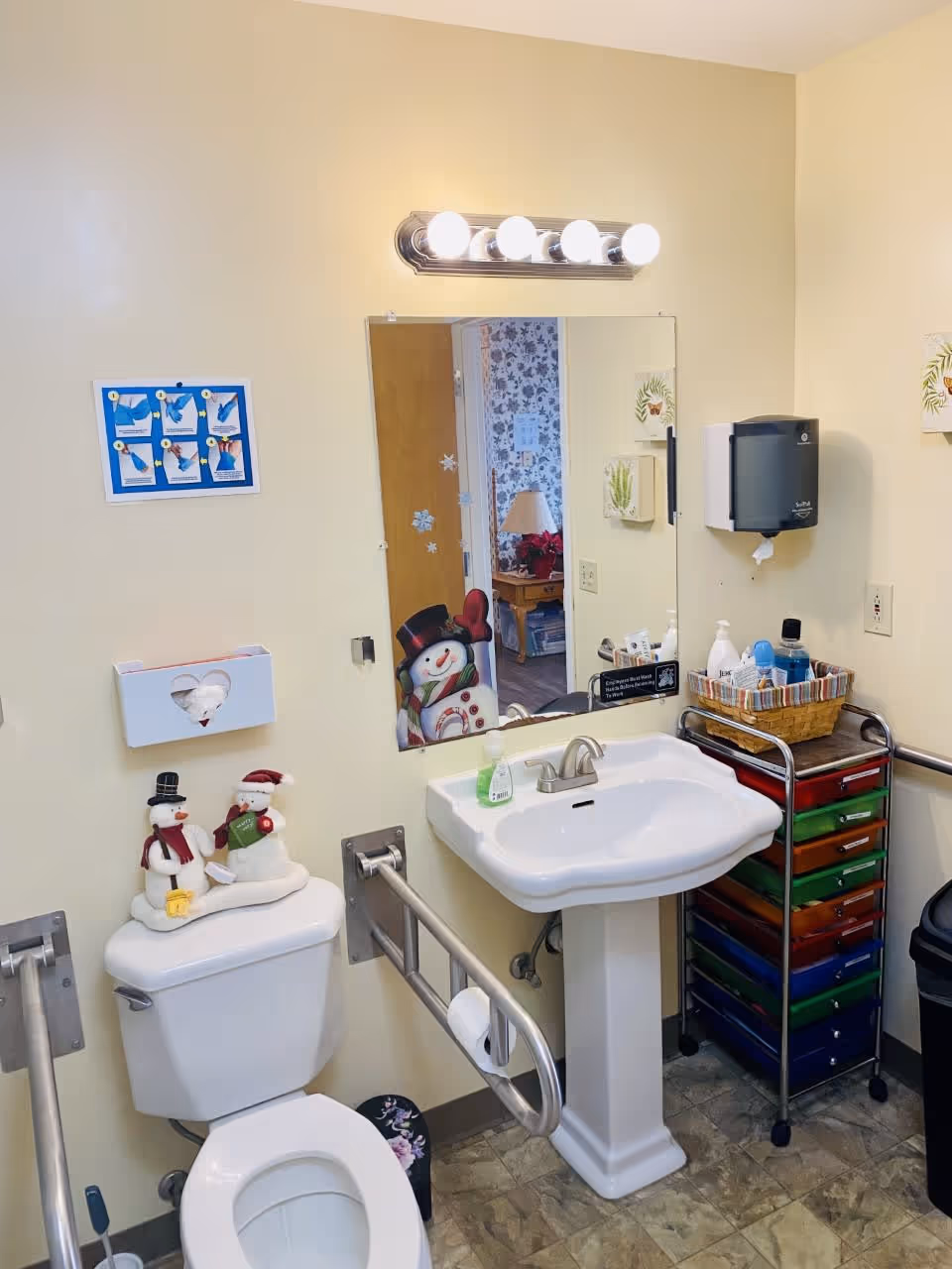 Accessible bathroom with a toilet, pedestal sink, mirror, grab bars and festive snowman decorations.