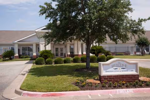 Exterior of a single-story senior living facility with a manicured lawn and brick sign.