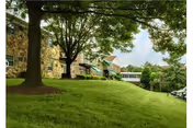 Stone-faced buildings on a grassy slope with large trees and a covered walkway.