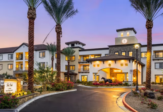 Front exterior view of The Park at Surprise independent living community with palm trees and driveway.