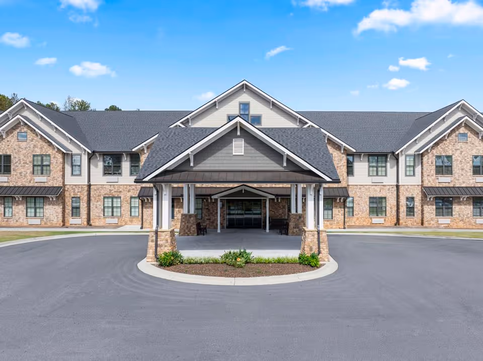 Front entrance of a two-story brick and siding residential building with a covered porte-cochère and circular driveway under a blue sky.