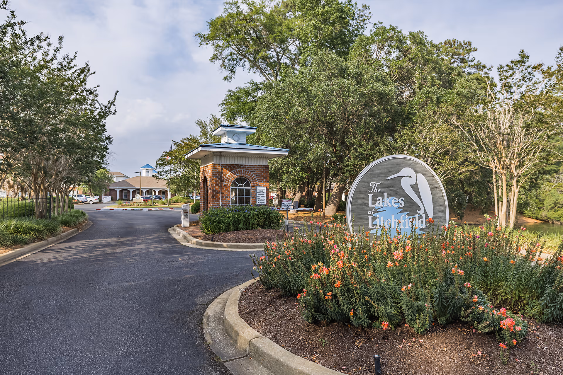 Entrance to The Lakes at Litchfield showing the round facility sign, flowerbed, a brick guardhouse, and the driveway.