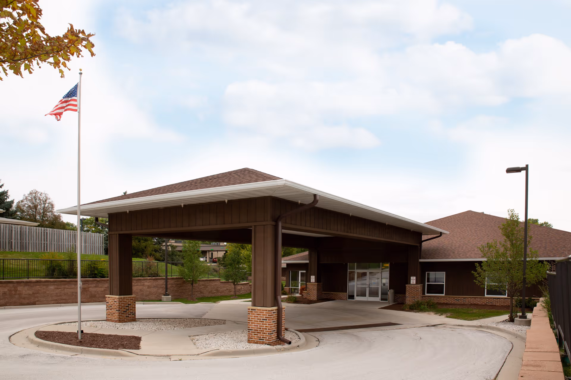 Front entrance of a single-story health facility with a covered drive-through canopy and an American flag.