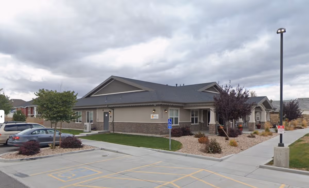 Single-story senior living facility building with parking spaces, landscaped entrance and cloudy sky.