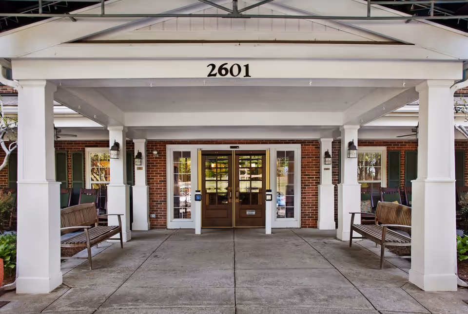 Covered entrance with white columns and benches leading to double glass doors beneath the number 2601.