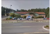 A single-story rehabilitation facility with a red roof beside a road and trees.