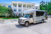 A shuttle van labeled 'The Trace' parked in front of a three-story white senior living building with columns and a tree-lined driveway.