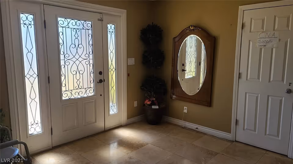 Entrance area with a decorative glass front door and sidelights, a wall-mounted oval mirror with a wooden frame, a potted plant in the corner, and a white door labeled 'CNA Supply'.