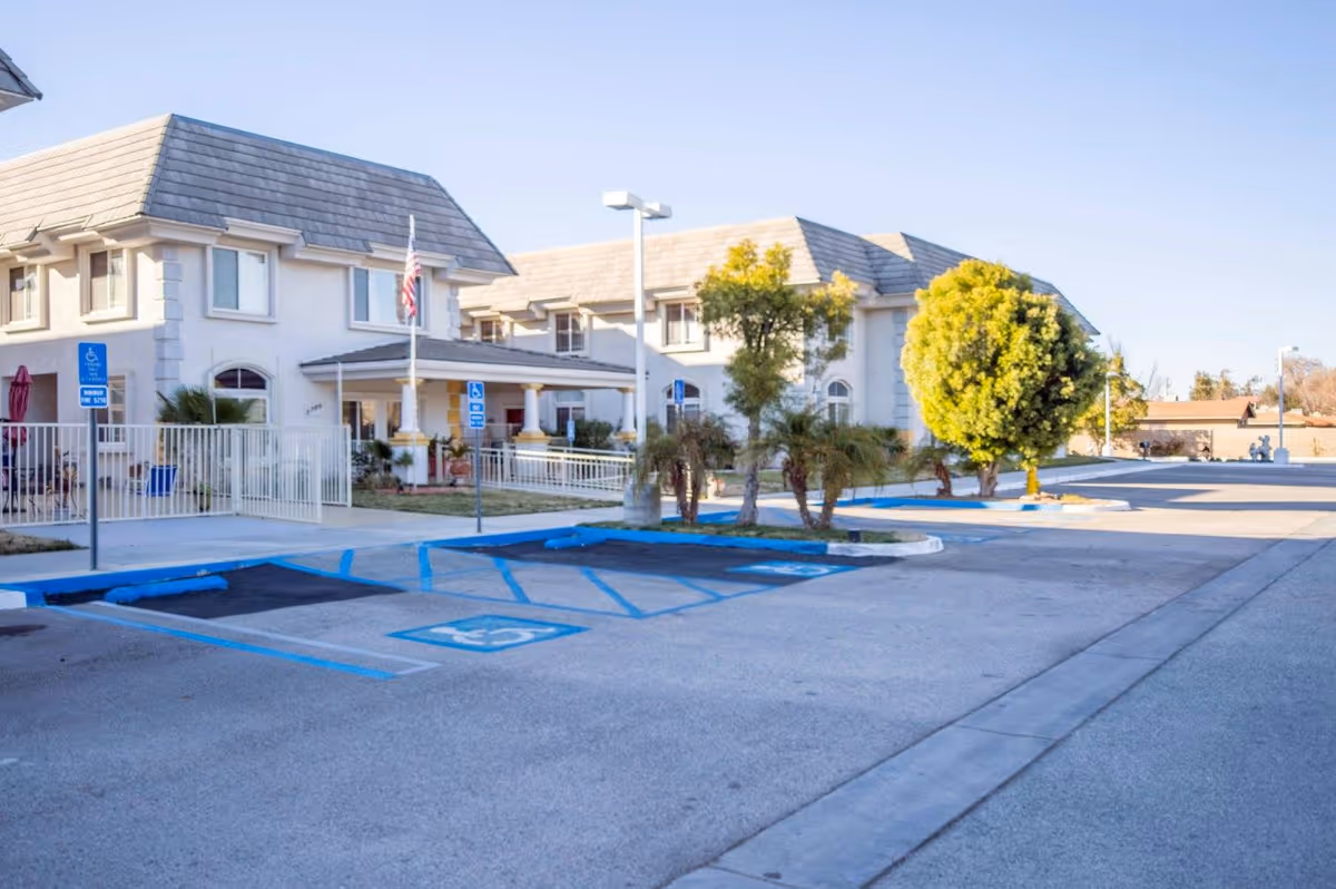 Front entrance and parking area of a two-story assisted living building with marked handicap parking spaces and an American flag.