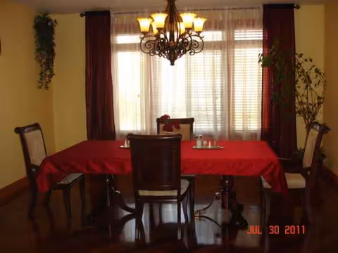 Dining room with a red tablecloth, chandelier, and empty chairs.