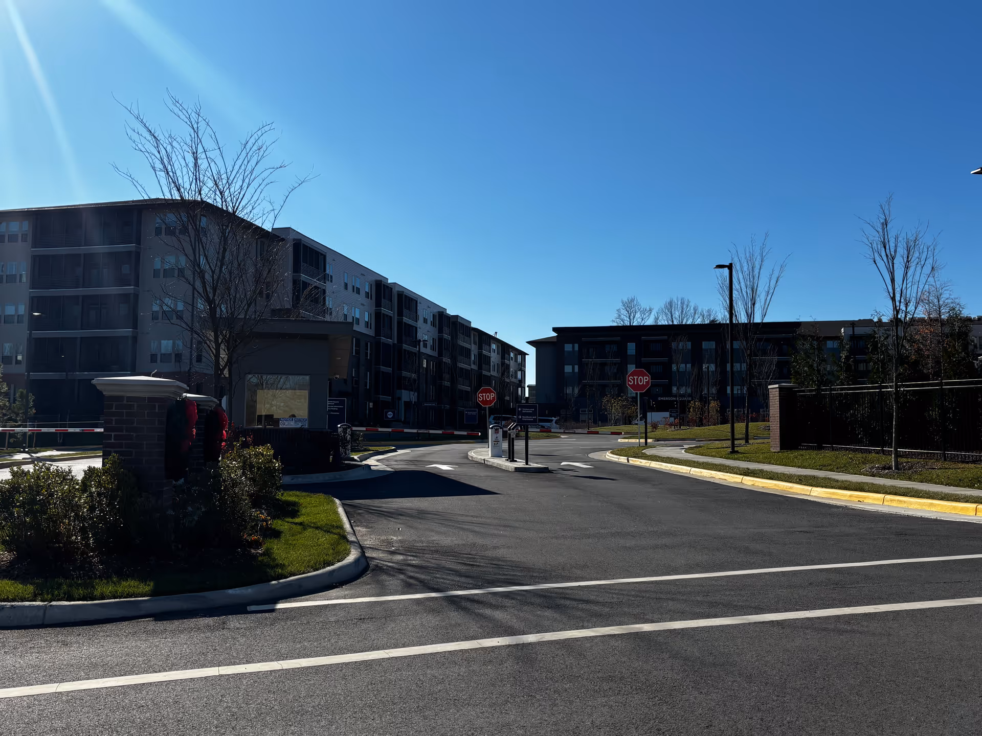 Entrance drive leading into a multi-story senior living complex with apartment buildings on either side under a clear blue sky.