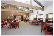 Spacious dining room with multiple wooden tables and chairs beneath exposed ceiling beams.