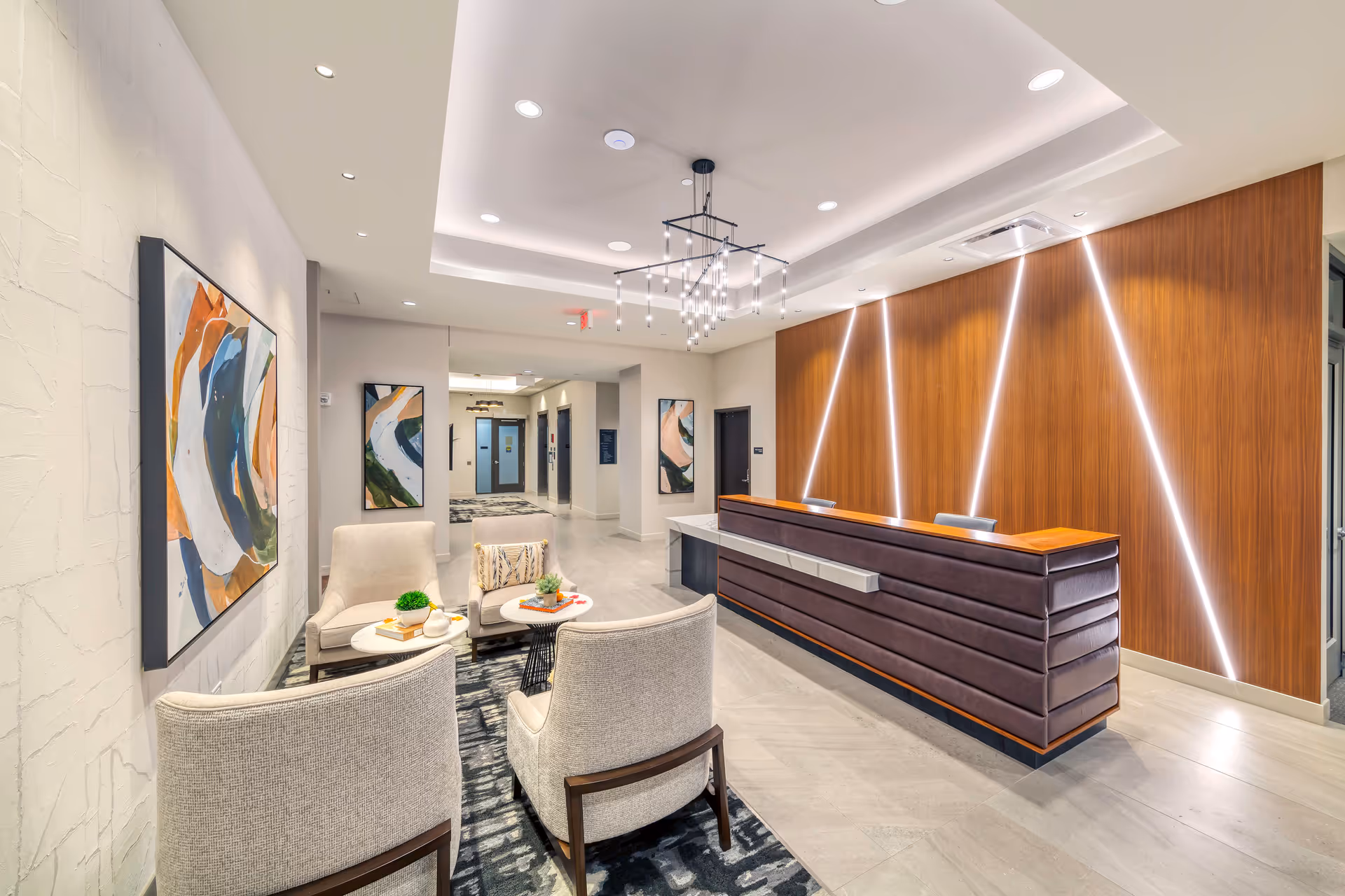 Modern reception lobby with a seating area, contemporary front desk, wood-paneled illuminated wall, and abstract artwork.