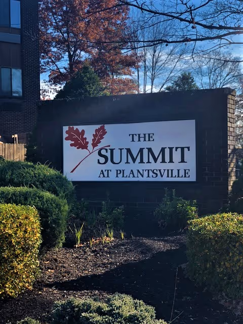 Brick entrance sign reading "The Summit at Plantsville" set among landscaped shrubs and trees.