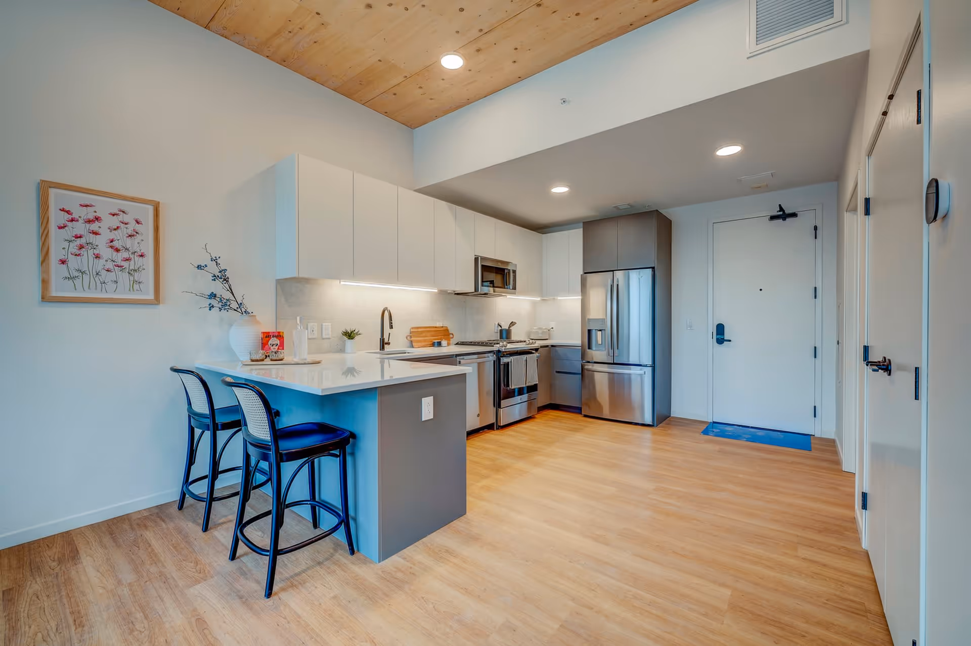 Modern open-concept kitchen with an island and two stools, stainless steel appliances, and wood flooring.