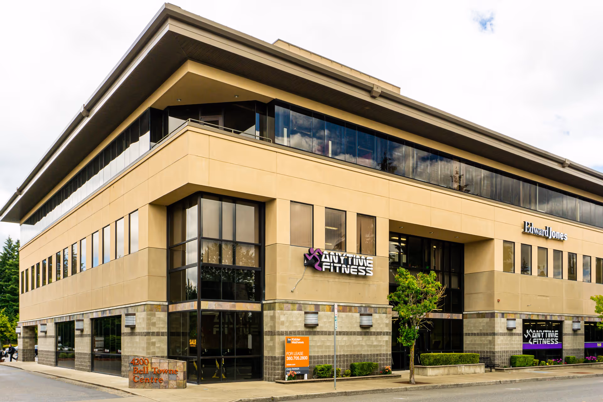 Street-level view of a modern multi-story commercial building with Anytime Fitness and Edward Jones signage.