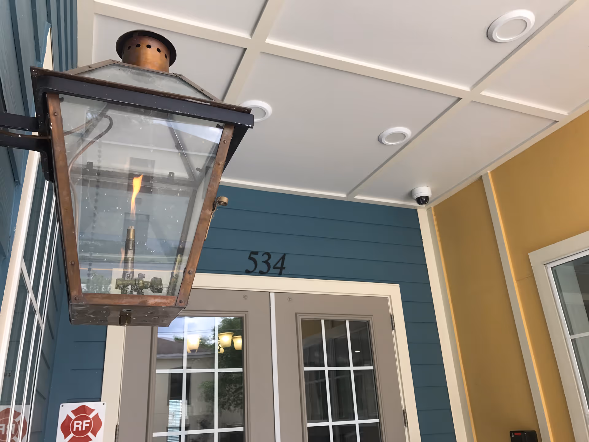 Covered building entrance with a large hanging lantern, double glass-paneled doors numbered 534, teal siding and yellow trim.