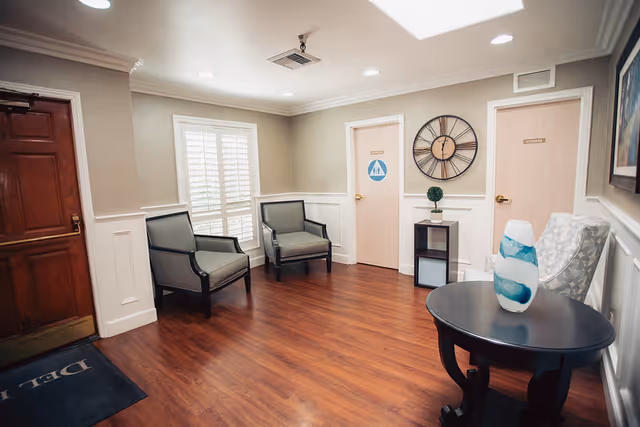 A small reception/waiting area with armchairs, a round table holding a decorative vase, a wall clock, and two doors.