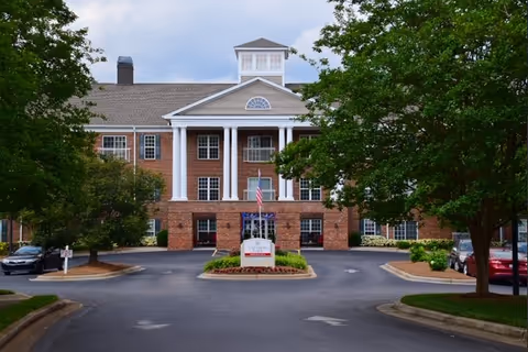Brick senior living facility with a circular driveway and trees.