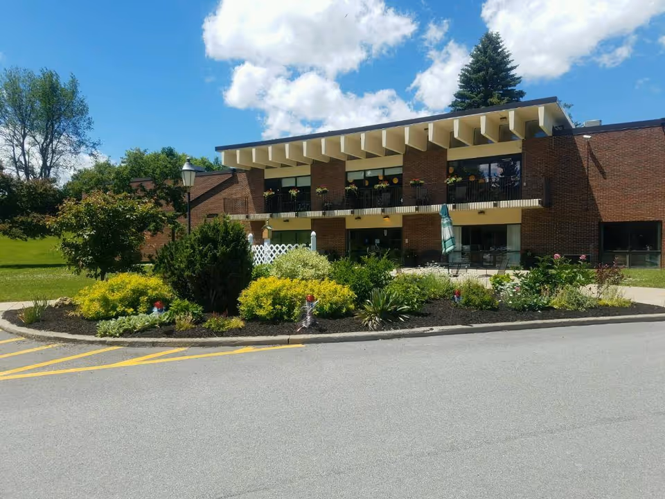 Two-story brick building with balconies, landscaped planting bed and a circular driveway under a blue sky.