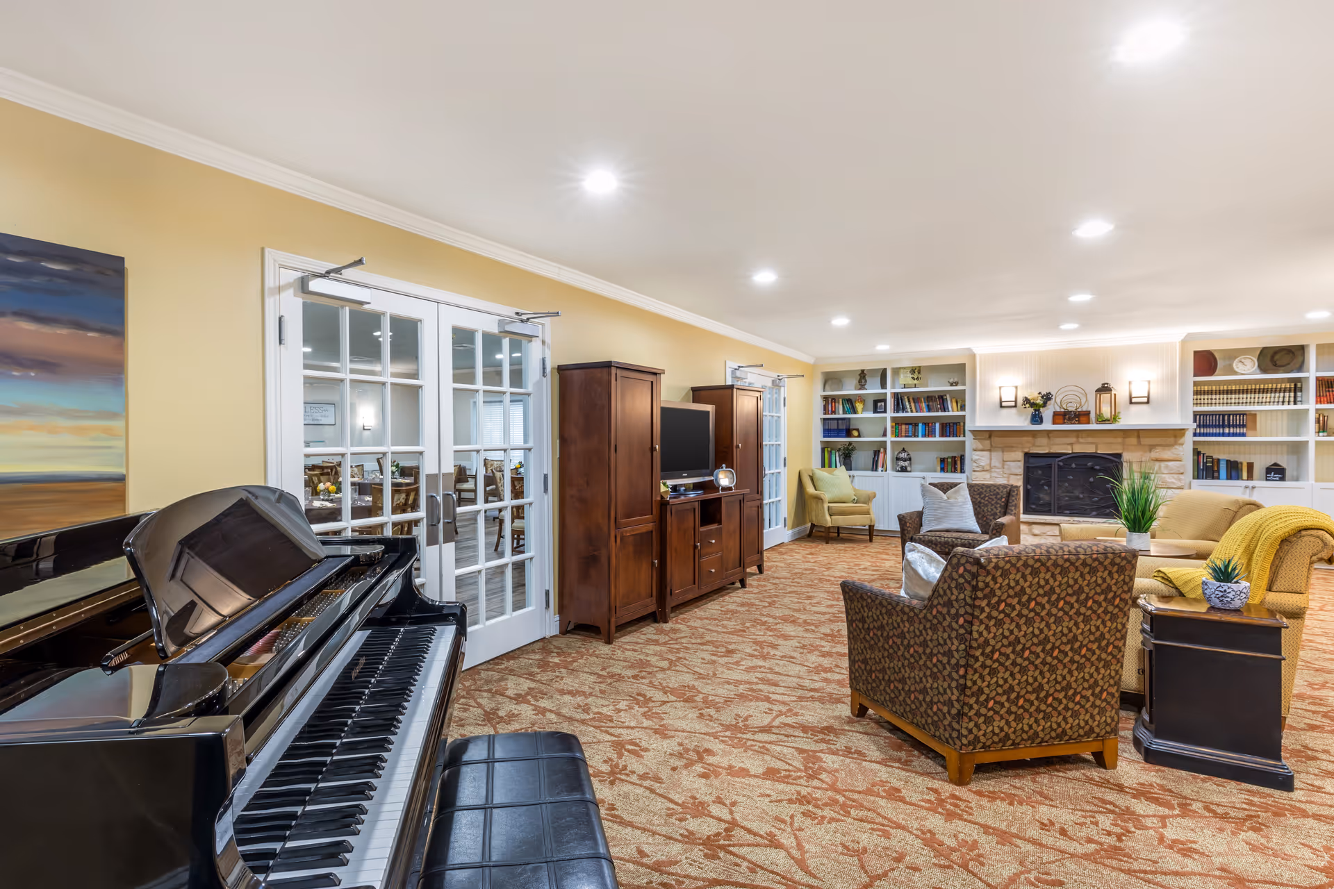 Bright communal living room with a grand piano, seating area, fireplace and bookshelves.